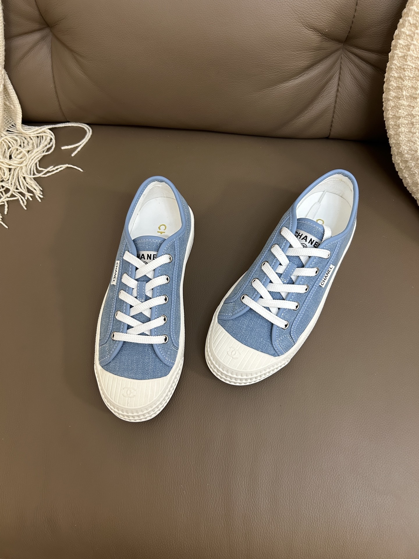 A pair of Chanel light blue denim low-top sneakers with white laces and embossed CC logo on the toe cap. - Hình 7