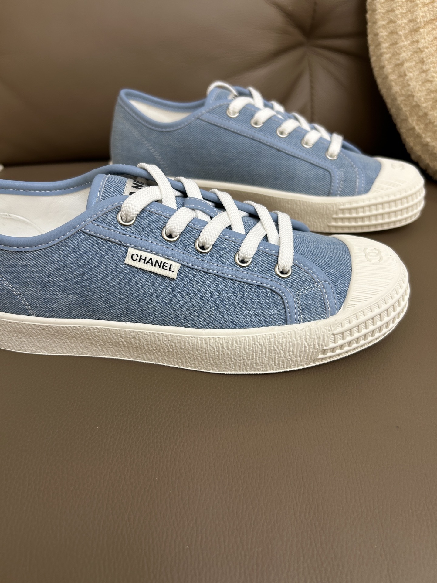A pair of Chanel light blue denim low-top sneakers with white laces and embossed CC logo on the toe cap. - Hình 6