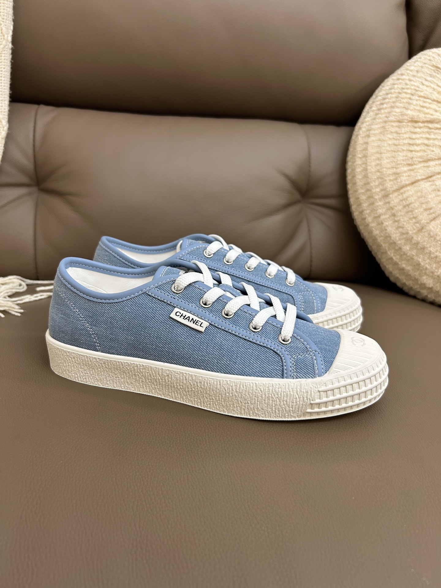 A pair of Chanel light blue denim low-top sneakers with white laces and embossed CC logo on the toe cap. - Hình 5