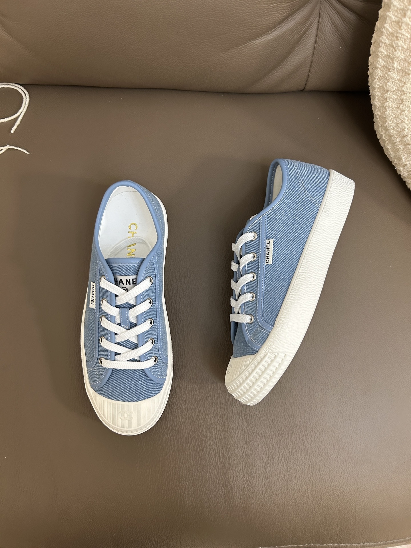 A pair of Chanel light blue denim low-top sneakers with white laces and embossed CC logo on the toe cap. - Hình 3
