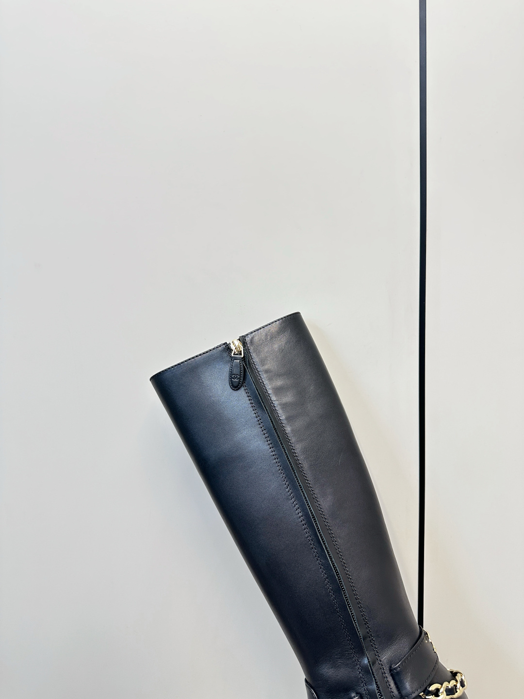 Pair of Chanel black leather knee-high boots with gold chain ankle detail on a wooden surface next to a Chanel shoe box. - Hình 9