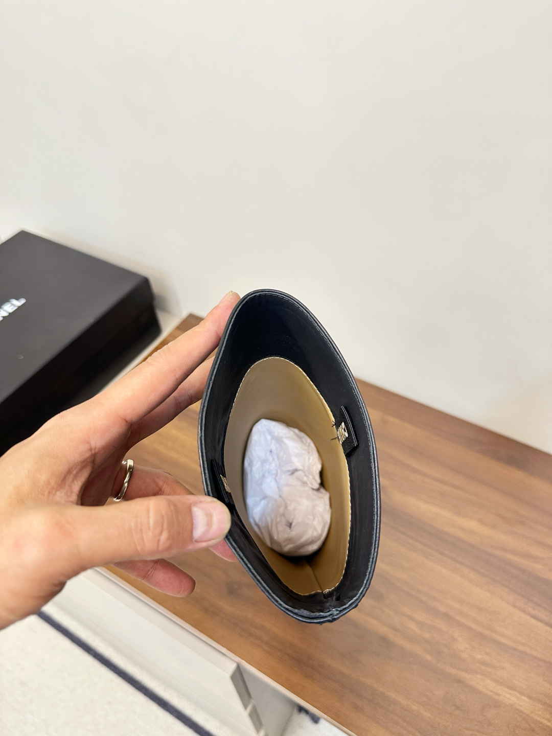 A pair of black Chanel knee-high leather riding boots featuring the embossed CC logo on the toe cap, displayed on a wooden surface next to a Chanel shoebox. - Hình 8