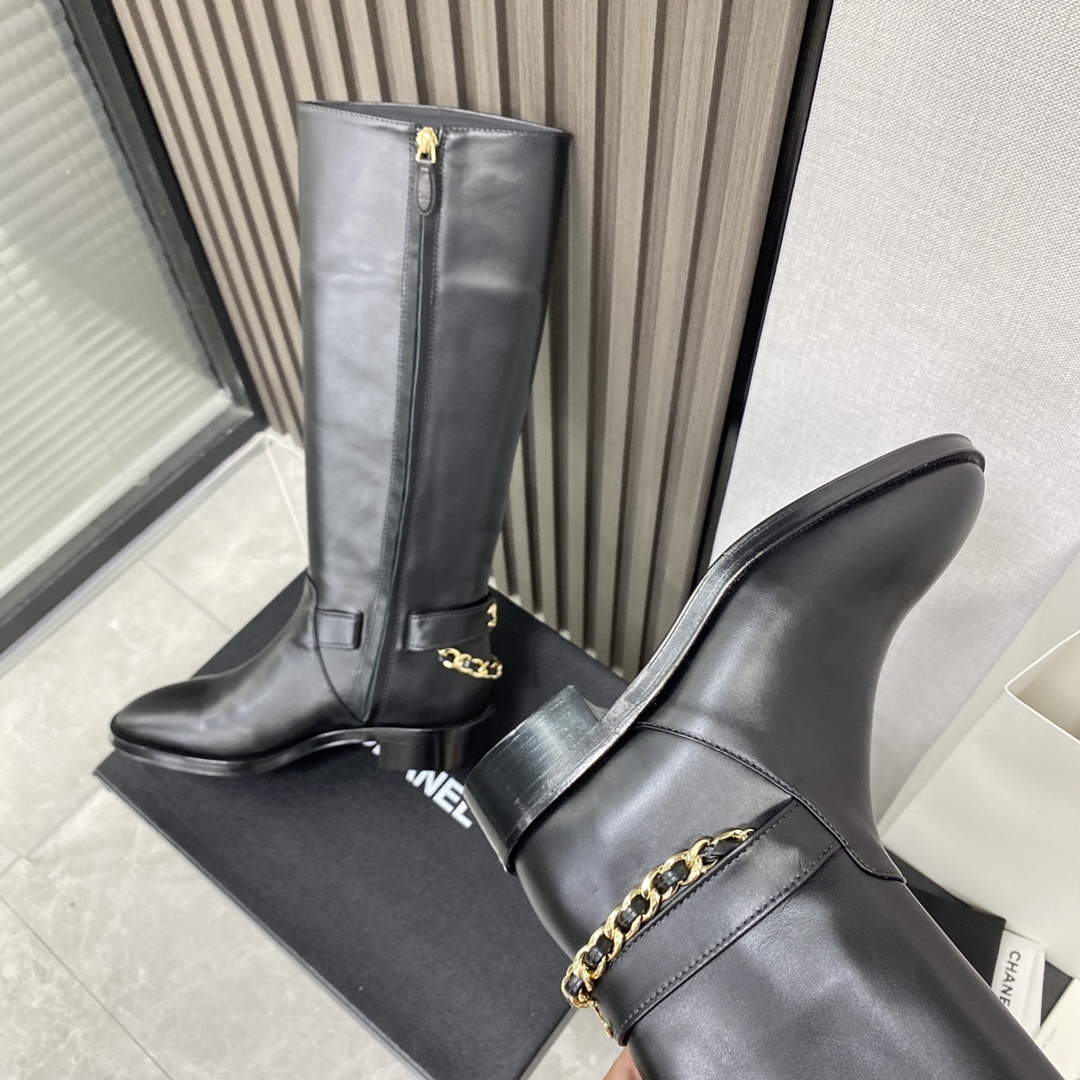 Pair of black leather knee-high boots with gold chain detail on a black designer box - Hình 7