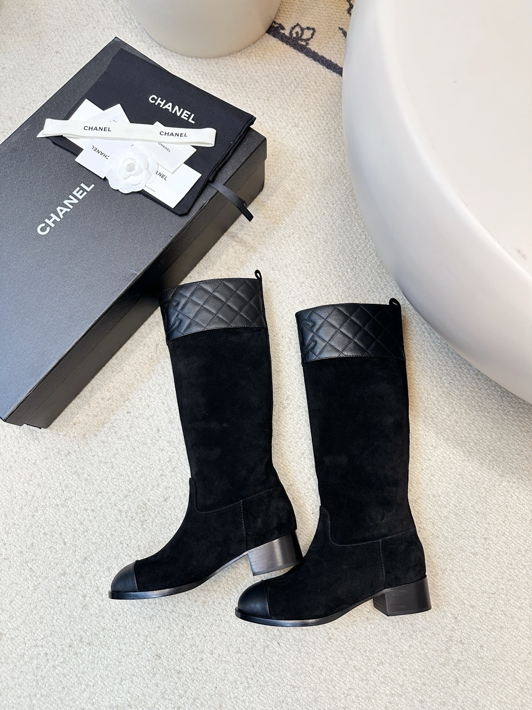 A pair of Chanel black suede knee-high boots with quilted leather tops and leather toe caps on a wooden surface. - Hình 9