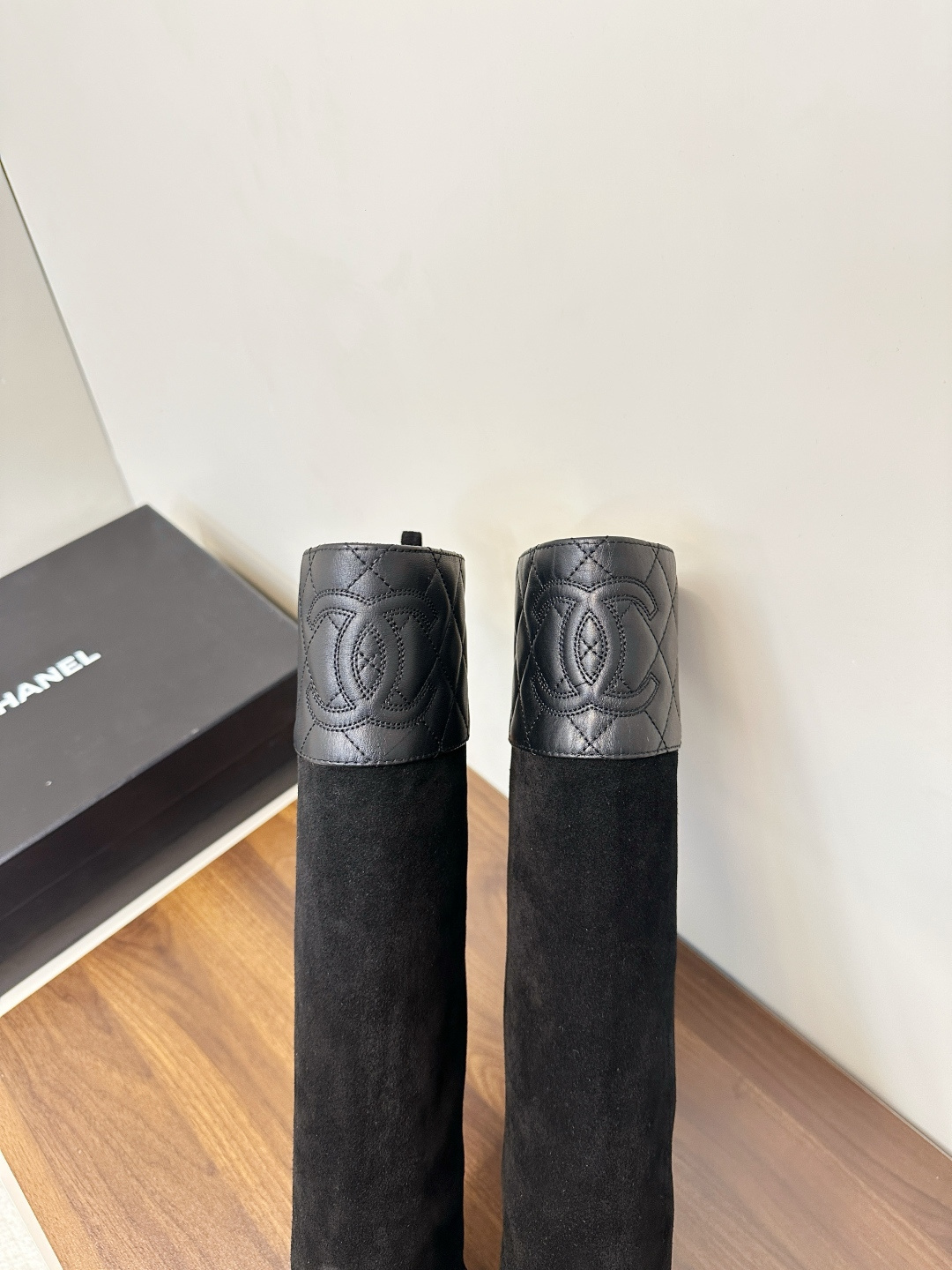 A pair of Chanel black suede knee-high boots with quilted leather tops and leather toe caps on a wooden surface. - Hình 8