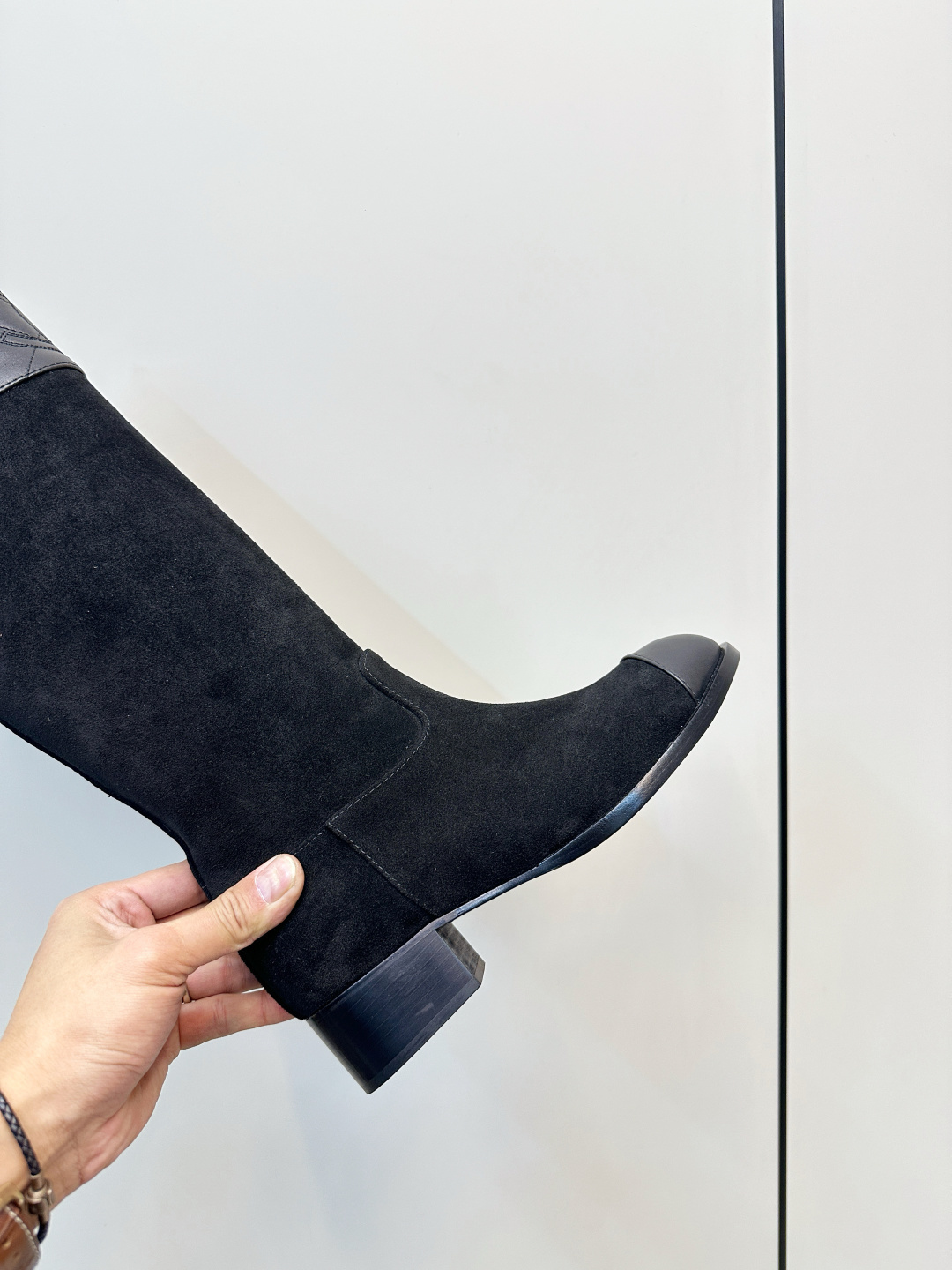 A pair of Chanel black suede knee-high boots with quilted leather tops and leather toe caps on a wooden surface. - Hình 7