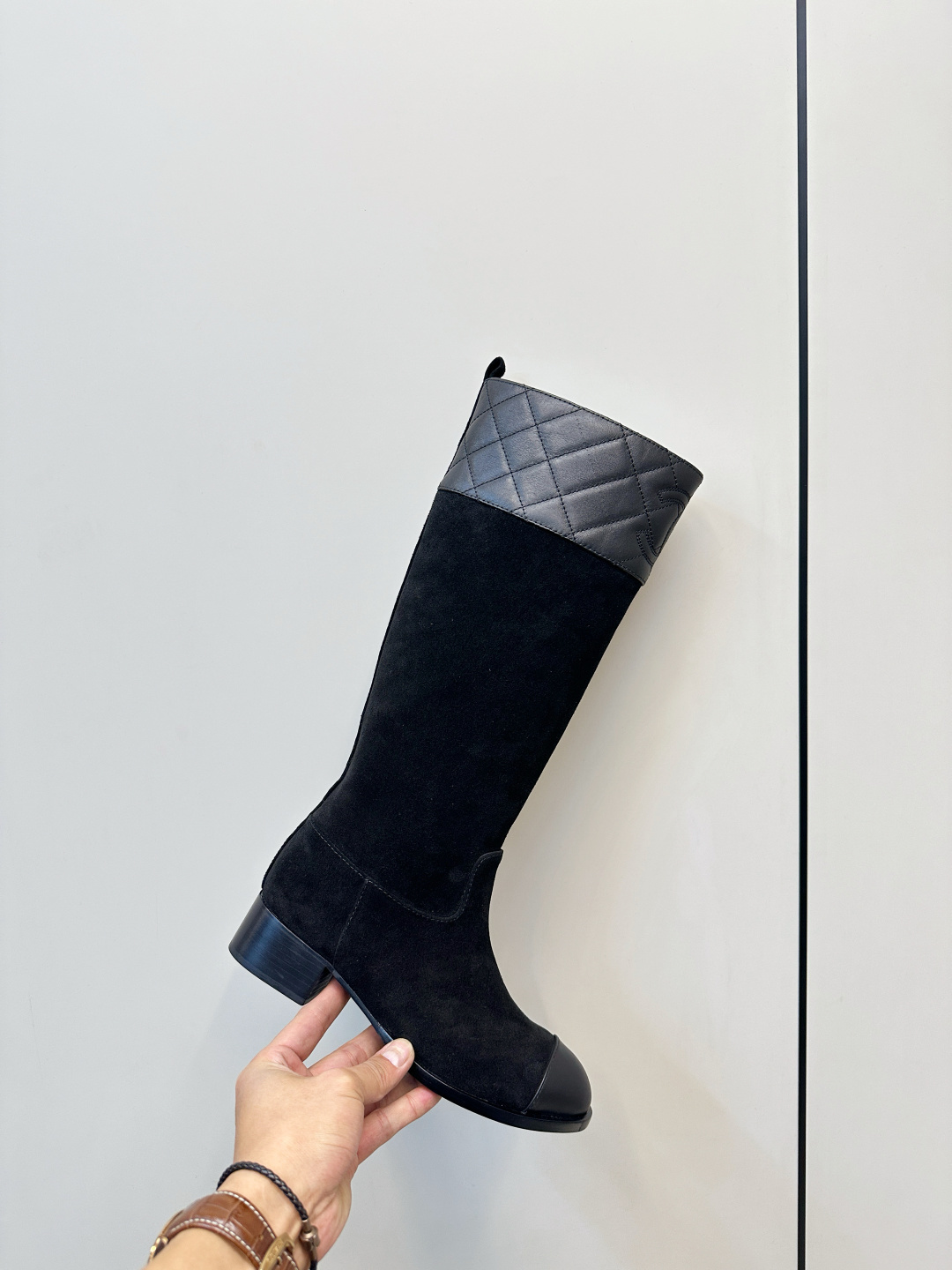 A pair of Chanel black suede knee-high boots with quilted leather tops and leather toe caps on a wooden surface. - Hình 6
