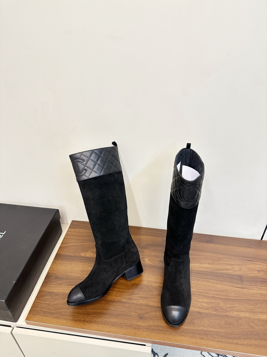 A pair of Chanel black suede knee-high boots with quilted leather tops and leather toe caps on a wooden surface. - Hình 5