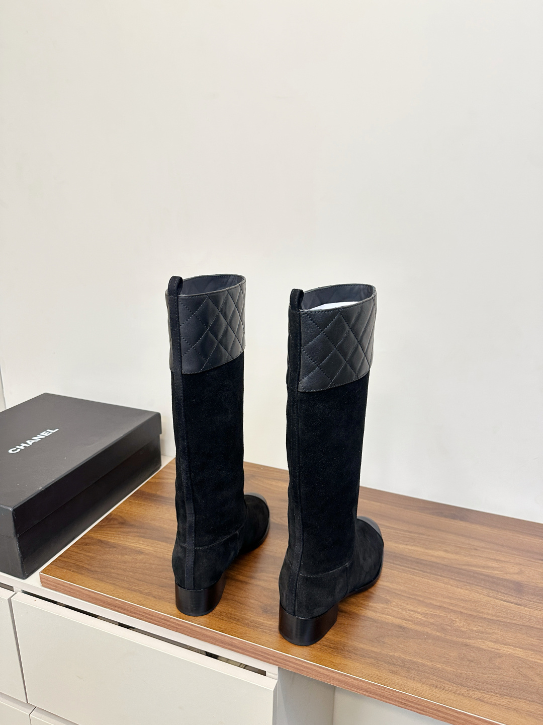 A pair of Chanel black suede knee-high boots with quilted leather tops and leather toe caps on a wooden surface. - Hình 4