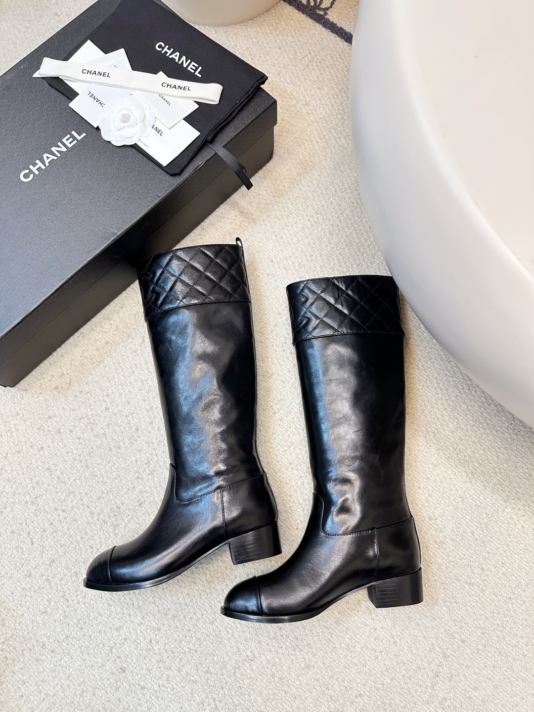 Pair of Chanel black quilted leather knee-high boots with embossed CC logo on a wooden surface. - Hình 9