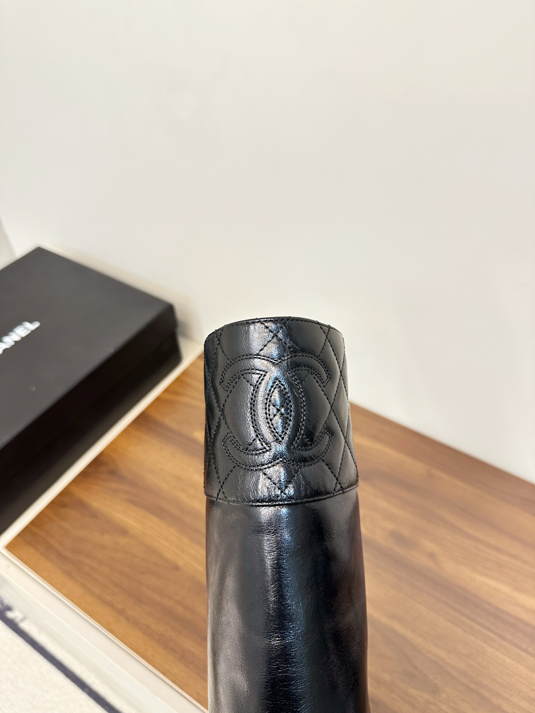 Pair of Chanel black quilted leather knee-high boots with embossed CC logo on a wooden surface. - Hình 8