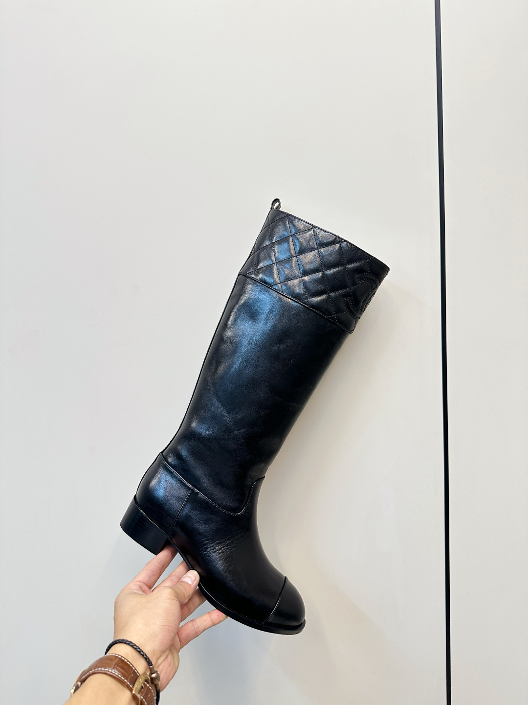 Pair of Chanel black quilted leather knee-high boots with embossed CC logo on a wooden surface. - Hình 6