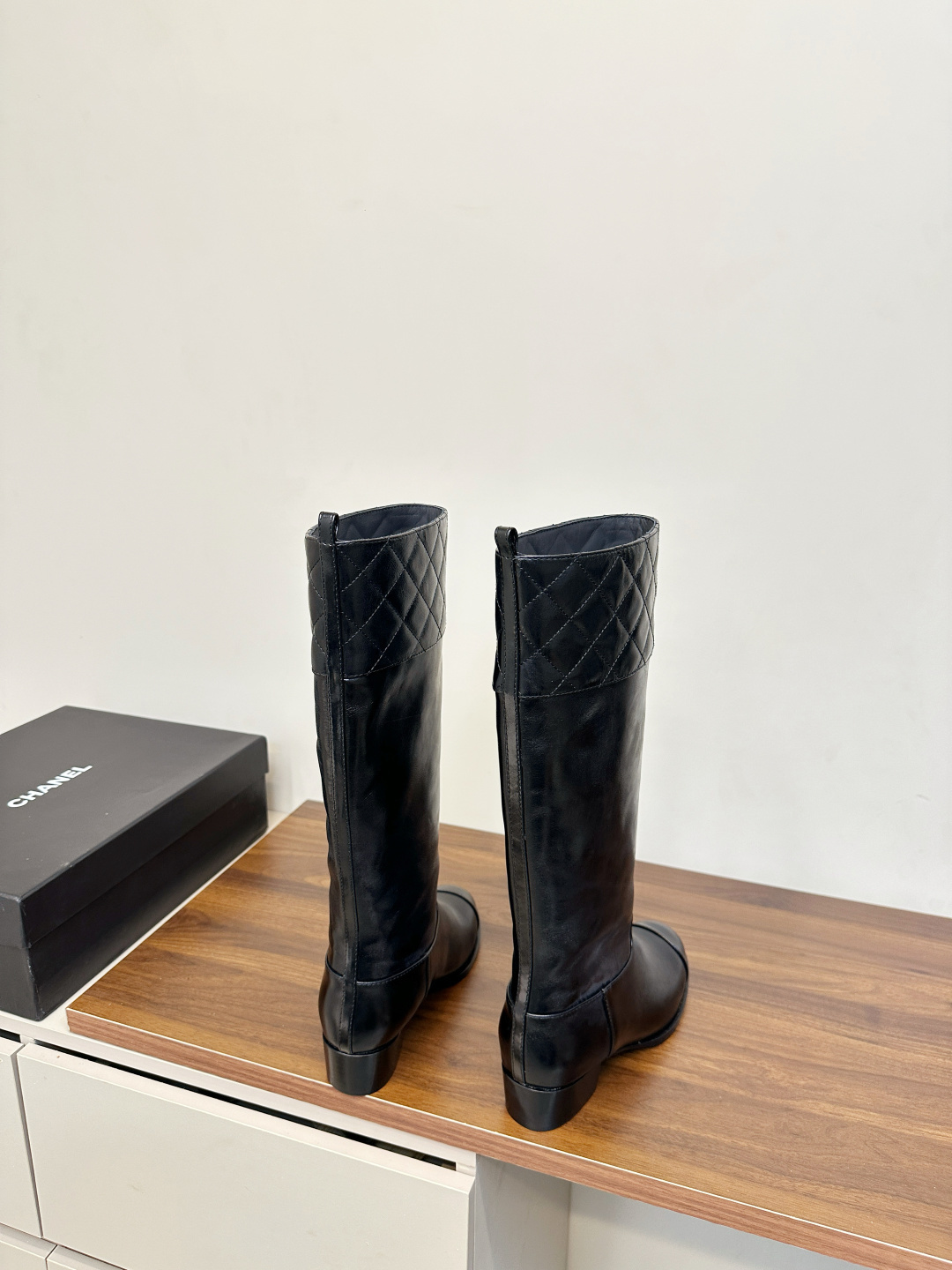 Pair of Chanel black quilted leather knee-high boots with embossed CC logo on a wooden surface. - Hình 4