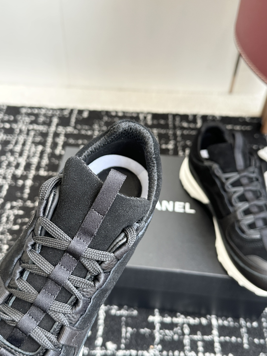 A pair of Chanel black suede and leather sneakers with white soles sitting on a Chanel designer box. - Hình 8