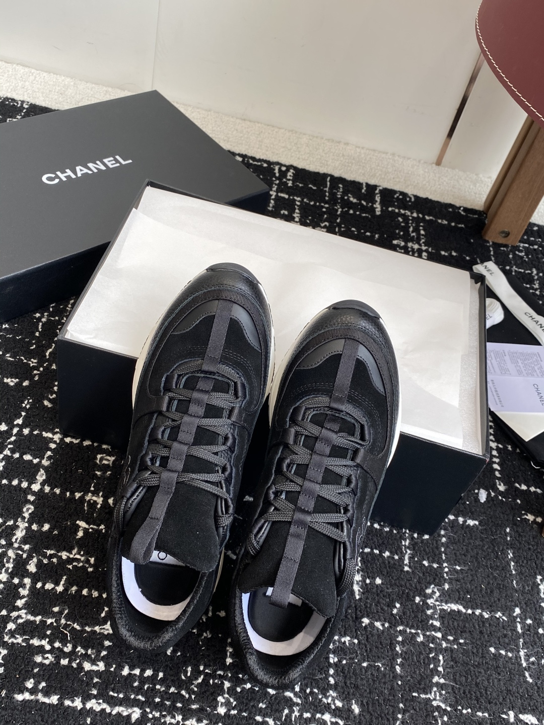 A pair of Chanel black suede and leather sneakers with white soles sitting on a Chanel designer box. - Hình 5