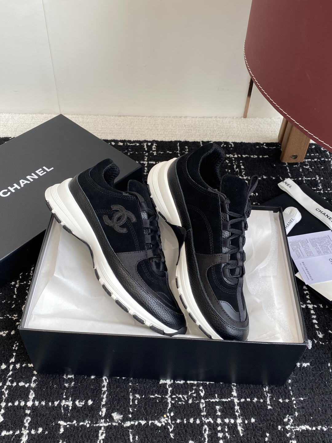A pair of Chanel black suede and leather sneakers with white soles sitting on a Chanel designer box. - Hình 4