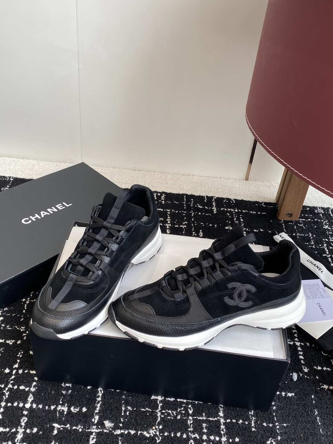A pair of Chanel black suede and leather sneakers with white soles sitting on a Chanel designer box. - Hình 3