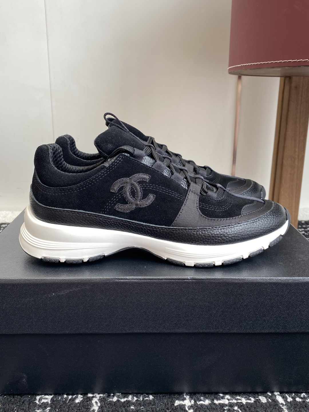 A pair of Chanel black suede and leather sneakers with white soles sitting on a Chanel designer box. - Hình 2