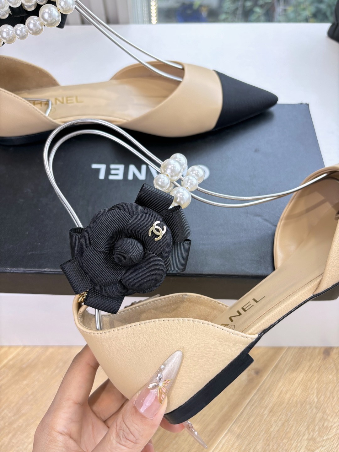 Elegant beige pointed-toe flats with black tips, featuring double-layered pearl ankle straps and a black camellia flower accent. - Hình 8