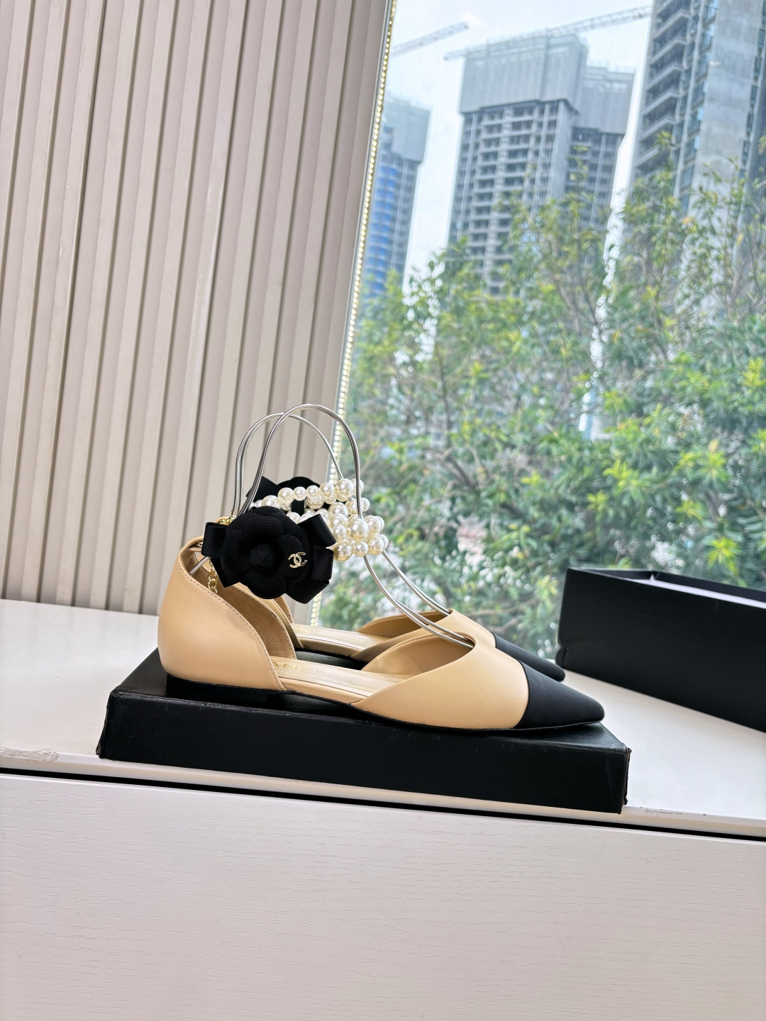 Elegant beige pointed-toe flats with black tips, featuring double-layered pearl ankle straps and a black camellia flower accent. - Hình 7