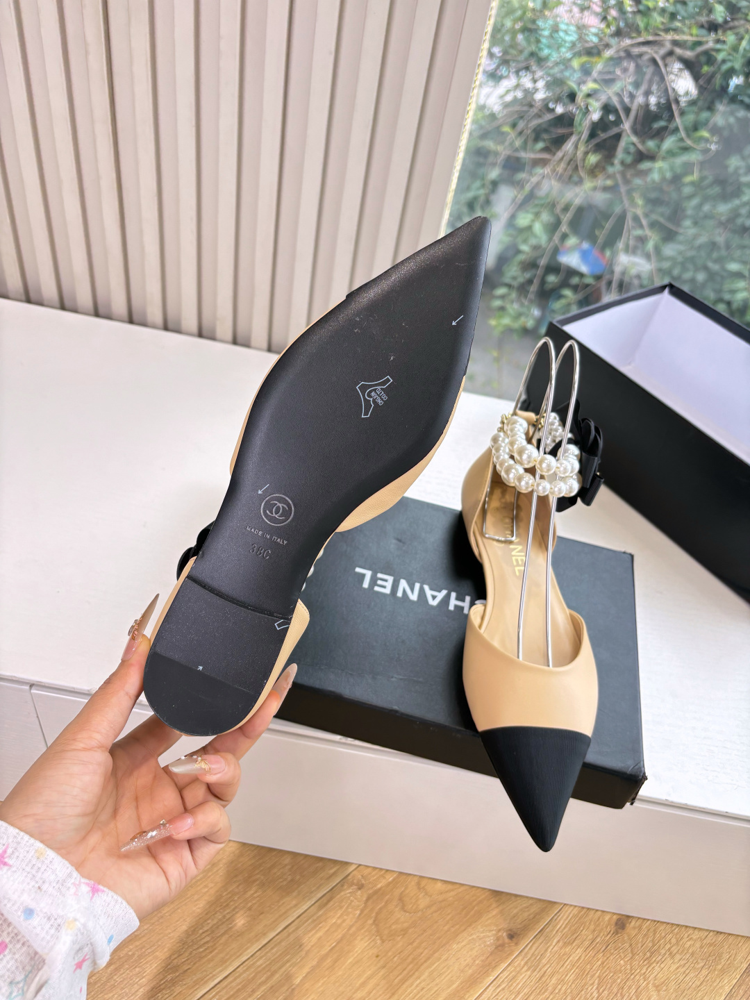 Elegant beige pointed-toe flats with black tips, featuring double-layered pearl ankle straps and a black camellia flower accent. - Hình 6