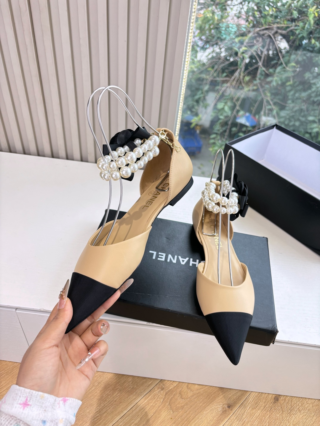 Elegant beige pointed-toe flats with black tips, featuring double-layered pearl ankle straps and a black camellia flower accent. - Hình 5