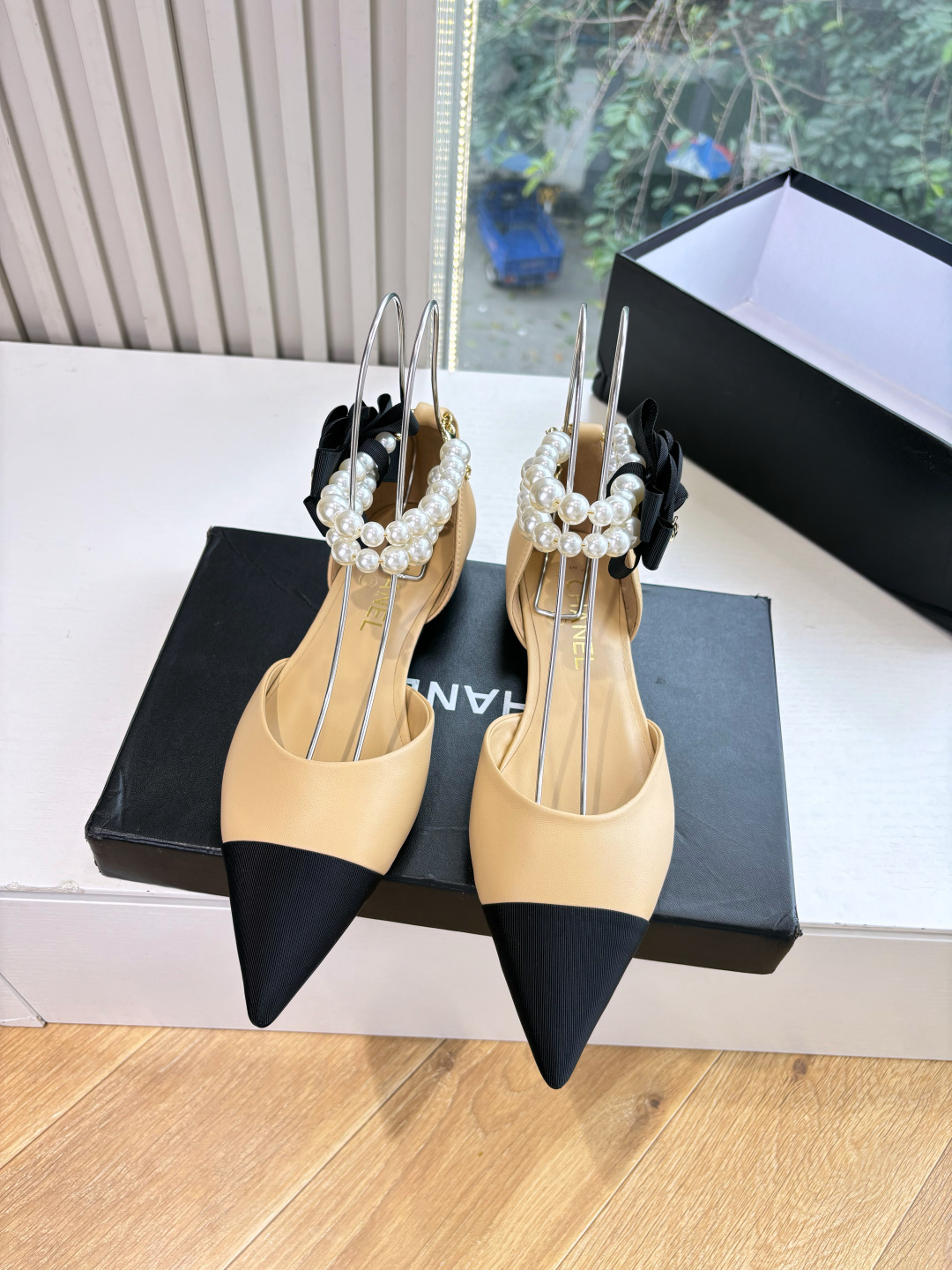 Elegant beige pointed-toe flats with black tips, featuring double-layered pearl ankle straps and a black camellia flower accent. - Hình 4