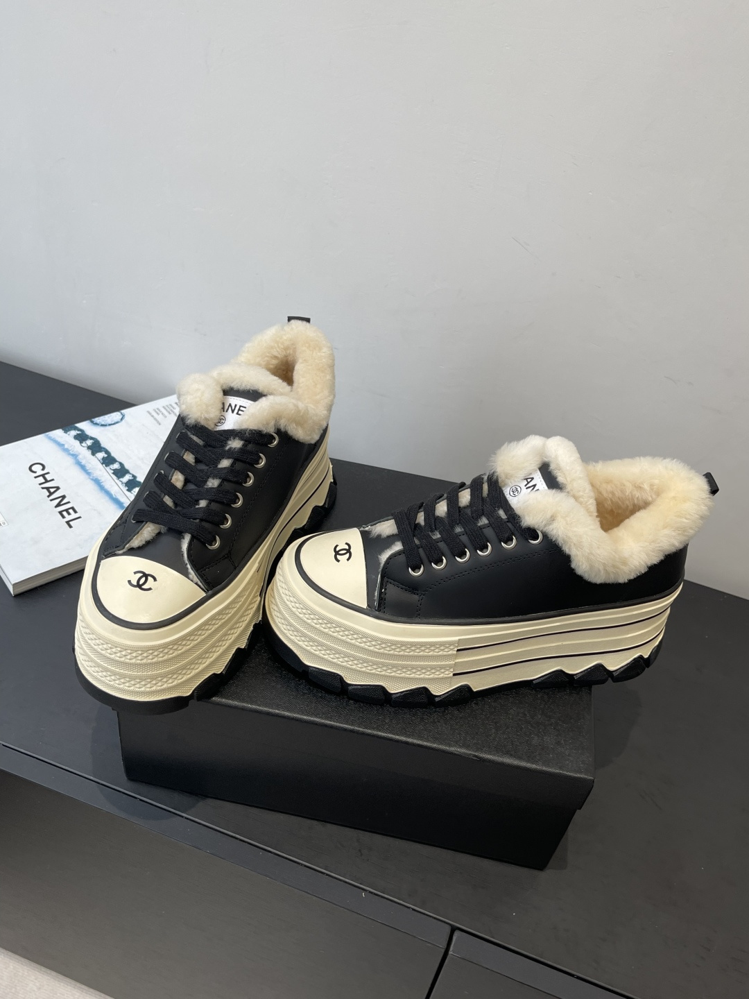 A pair of Chanel black leather platform sneakers with cream shearling lining and iconic CC logo on the toe cap, sitting on a black Chanel shoe box. - Hình 9