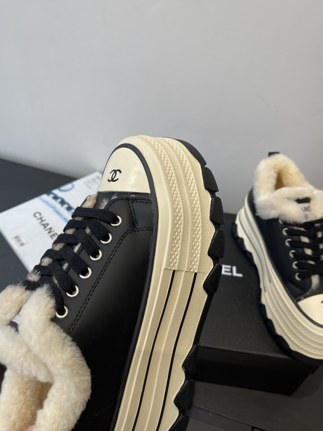A pair of Chanel black leather platform sneakers with cream shearling lining and iconic CC logo on the toe cap, sitting on a black Chanel shoe box. - Hình 7