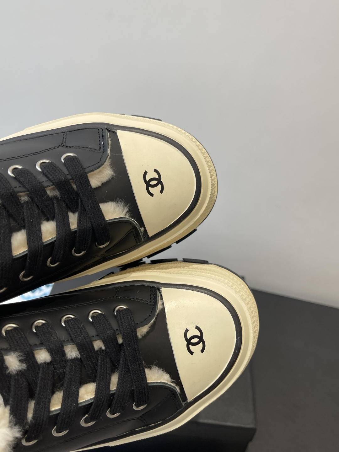 A pair of Chanel black leather platform sneakers with cream shearling lining and iconic CC logo on the toe cap, sitting on a black Chanel shoe box. - Hình 6