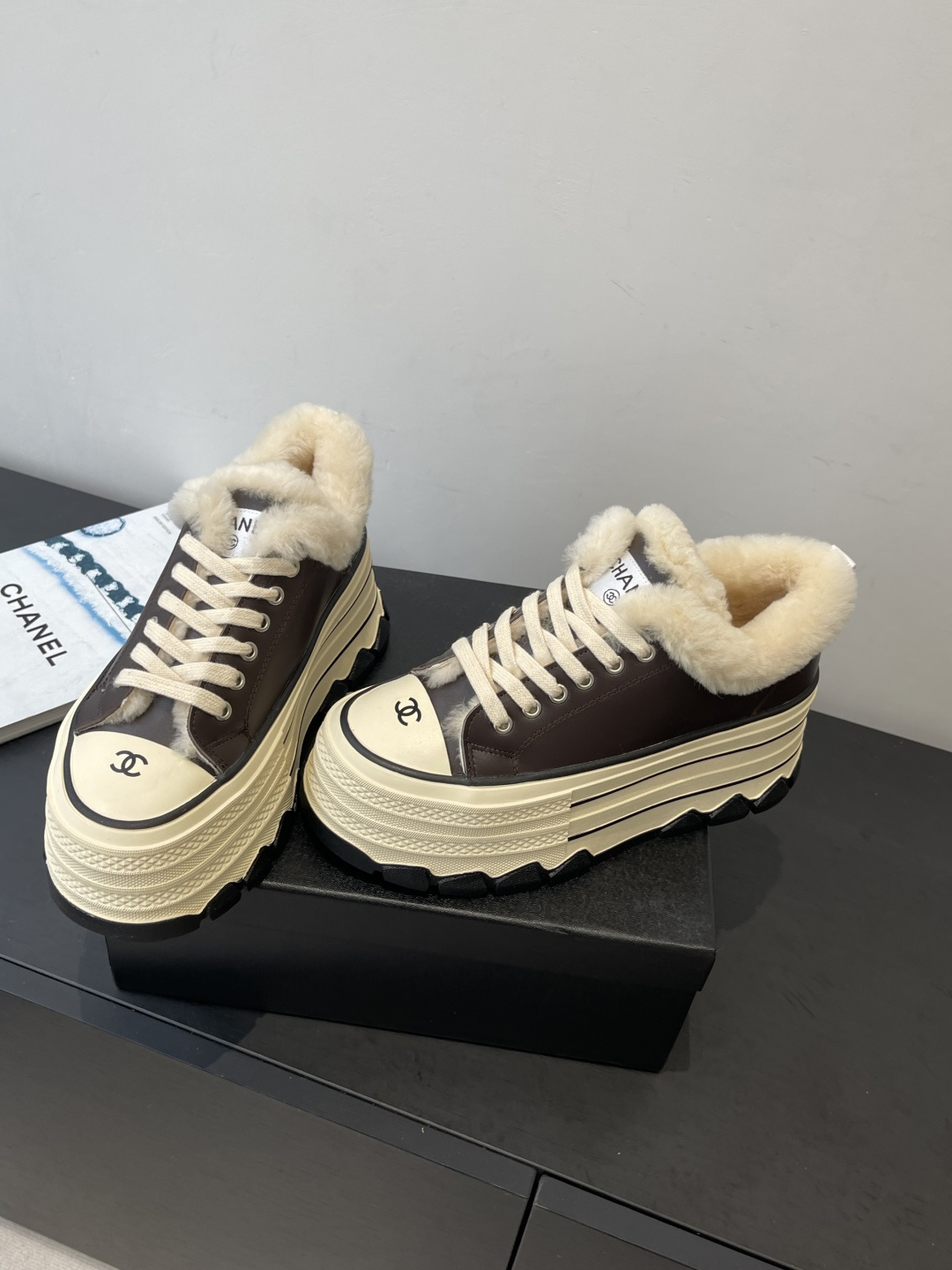 A pair of Chanel brown leather platform sneakers with white shearling lining and a thick cream-colored sole resting on a black Chanel box. - Hình 9