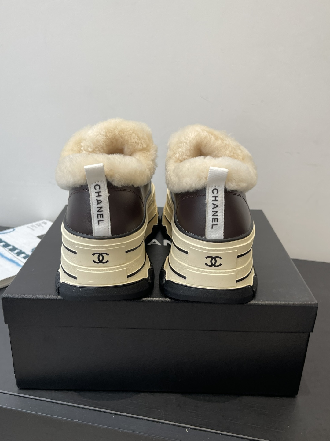 A pair of Chanel brown leather platform sneakers with white shearling lining and a thick cream-colored sole resting on a black Chanel box. - Hình 8