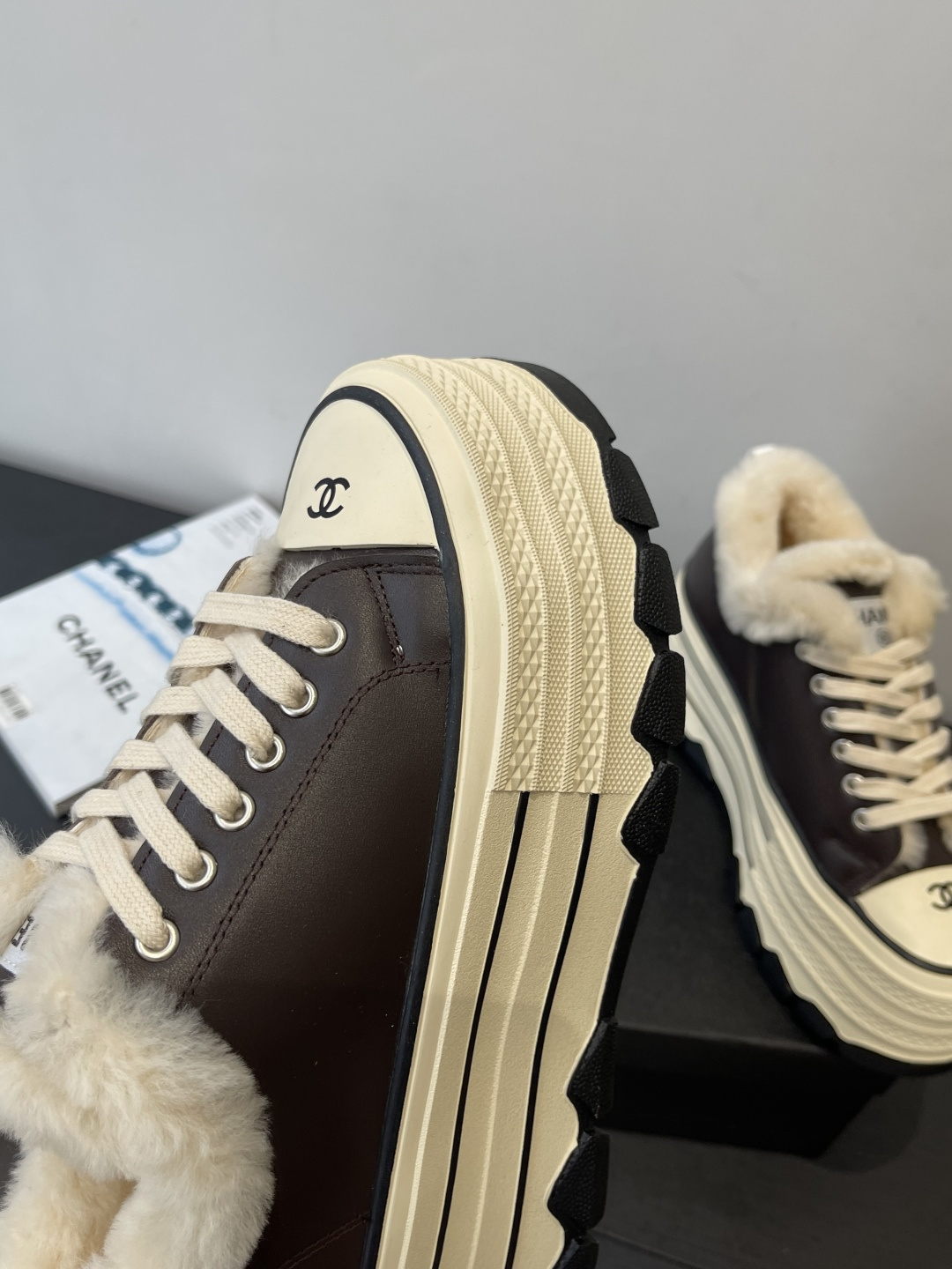A pair of Chanel brown leather platform sneakers with white shearling lining and a thick cream-colored sole resting on a black Chanel box. - Hình 7
