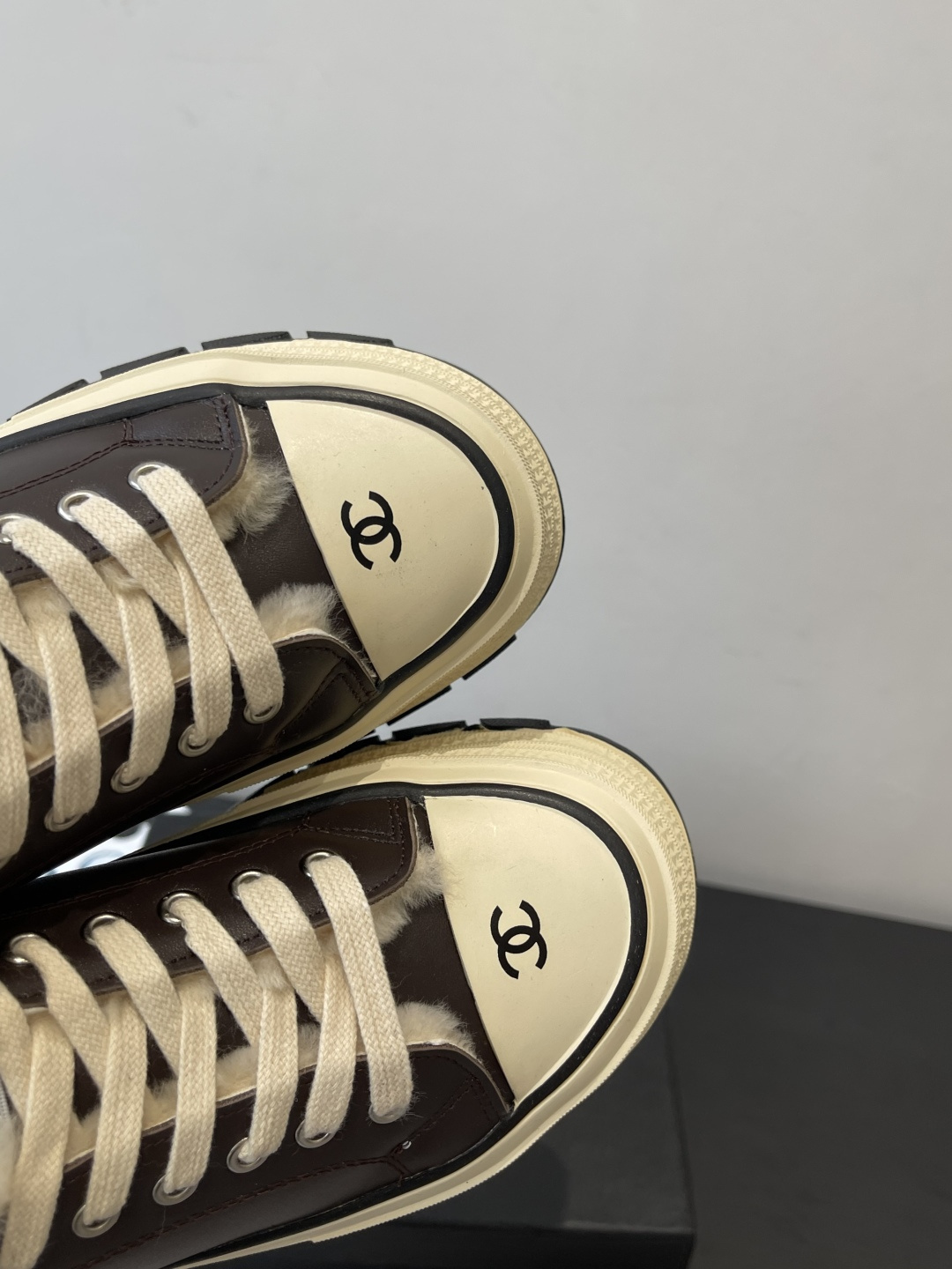 A pair of Chanel brown leather platform sneakers with white shearling lining and a thick cream-colored sole resting on a black Chanel box. - Hình 6