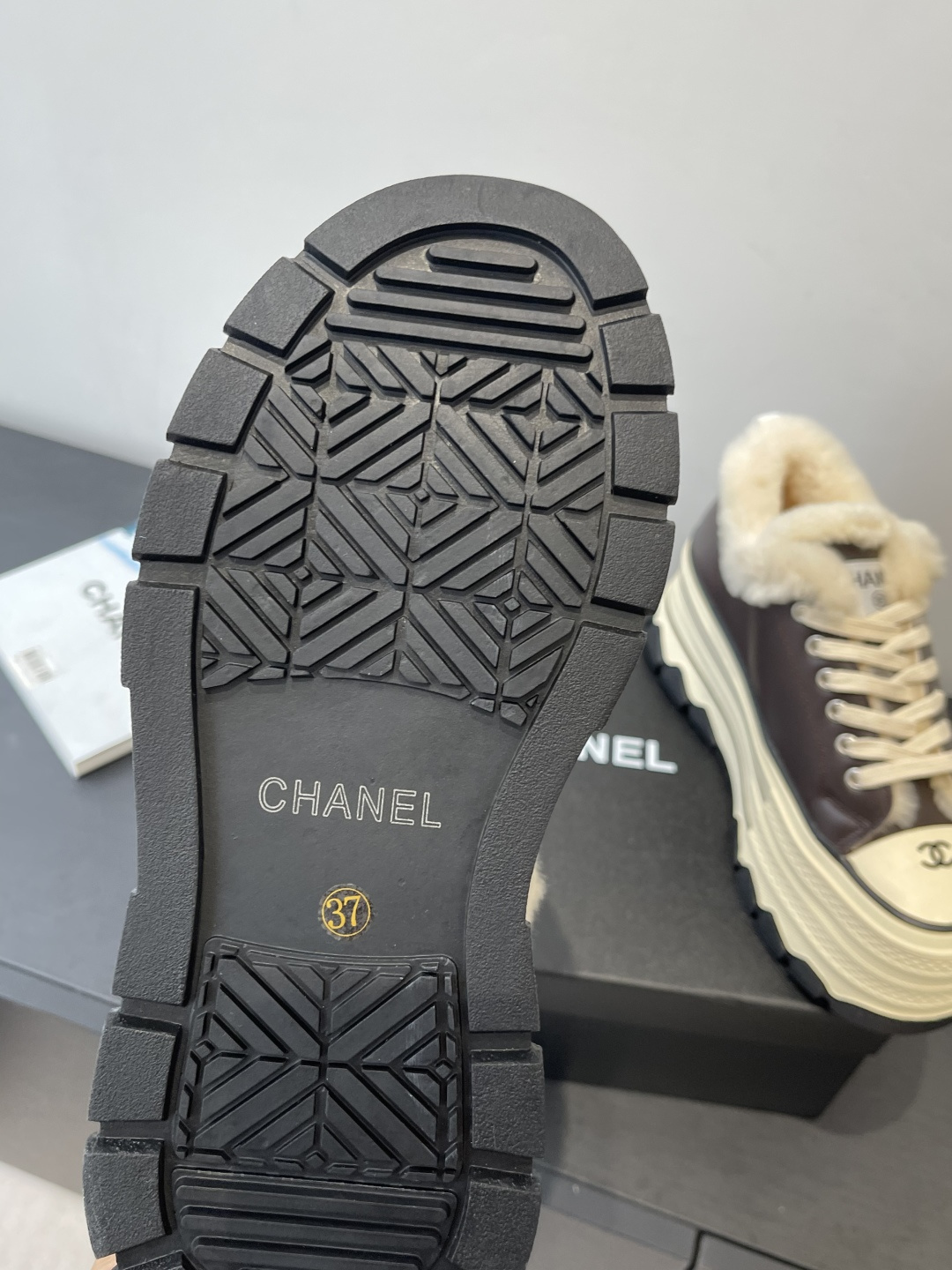 A pair of Chanel brown leather platform sneakers with white shearling lining and a thick cream-colored sole resting on a black Chanel box. - Hình 5