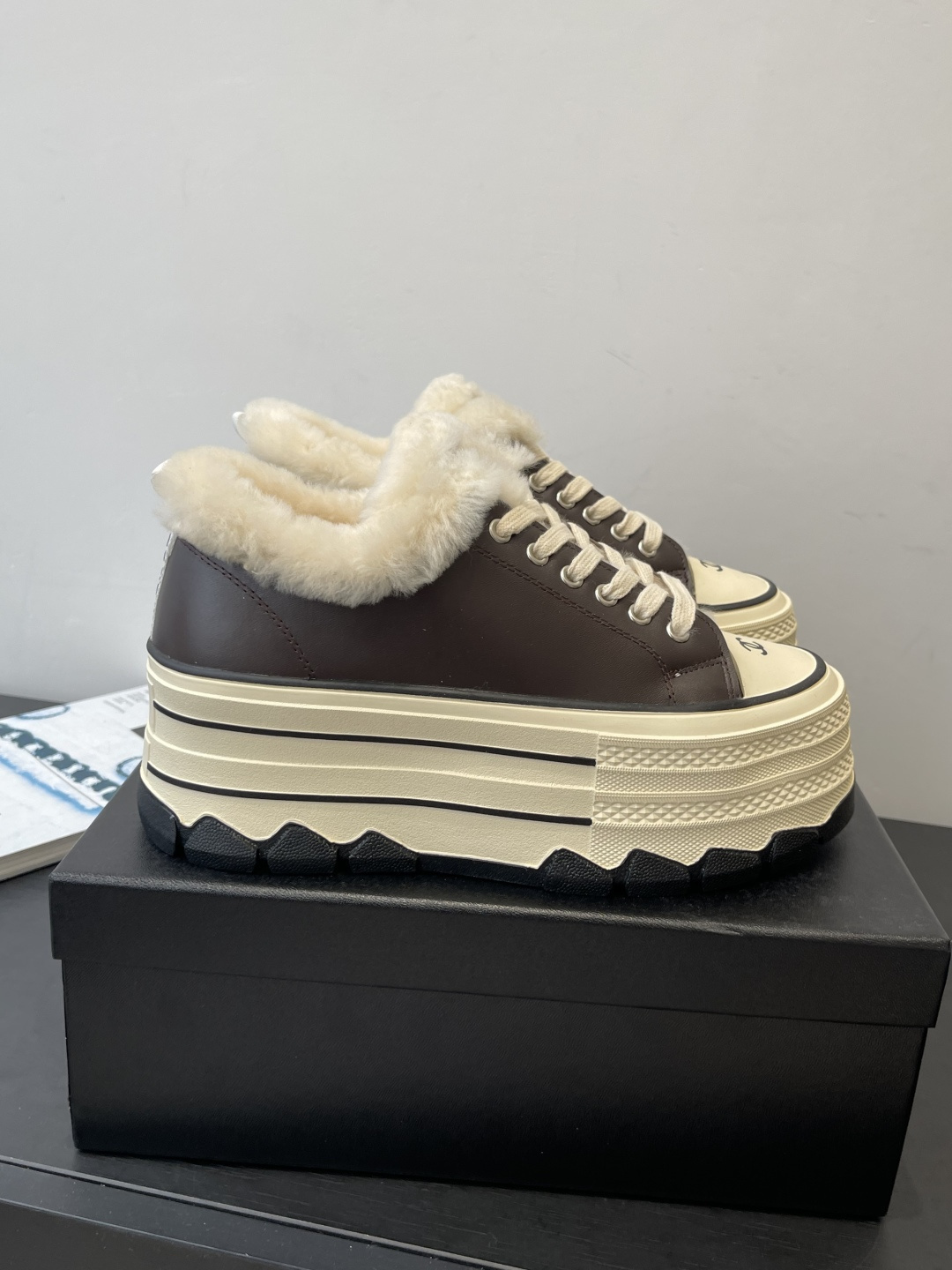 A pair of Chanel brown leather platform sneakers with white shearling lining and a thick cream-colored sole resting on a black Chanel box. - Hình 2