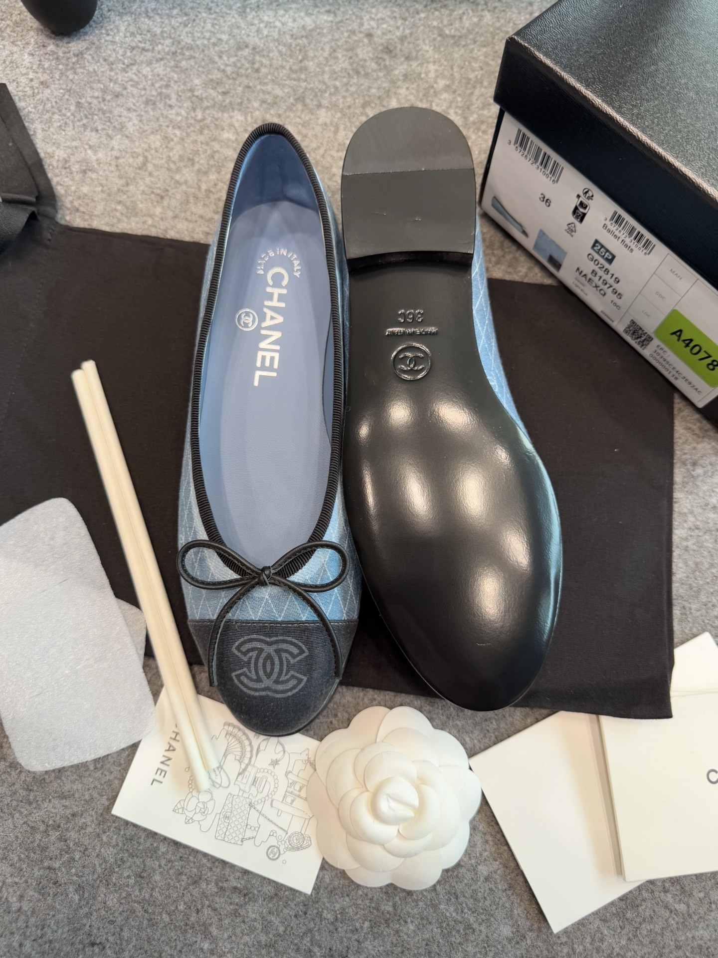 Pair of Chanel light blue quilted denim ballerina flats with black toe caps and bows inside a white luxury box. - Hình 10