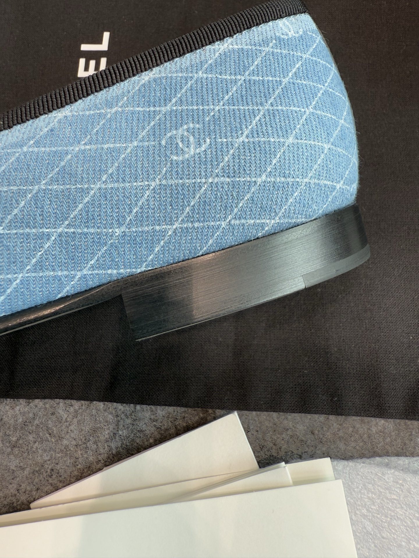 Pair of Chanel light blue quilted denim ballerina flats with black toe caps and bows inside a white luxury box. - Hình 8