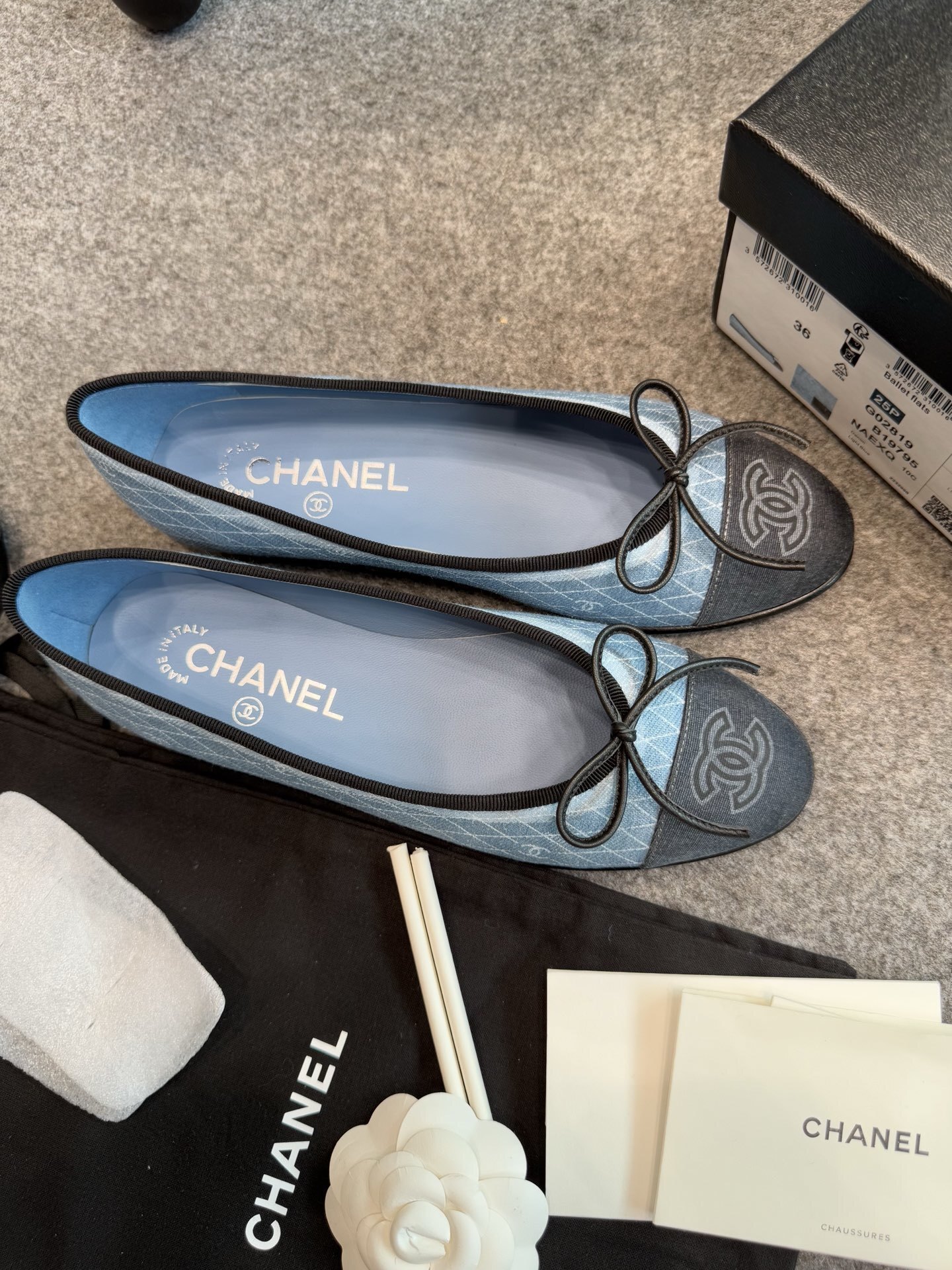 Pair of Chanel light blue quilted denim ballerina flats with black toe caps and bows inside a white luxury box. - Hình 7