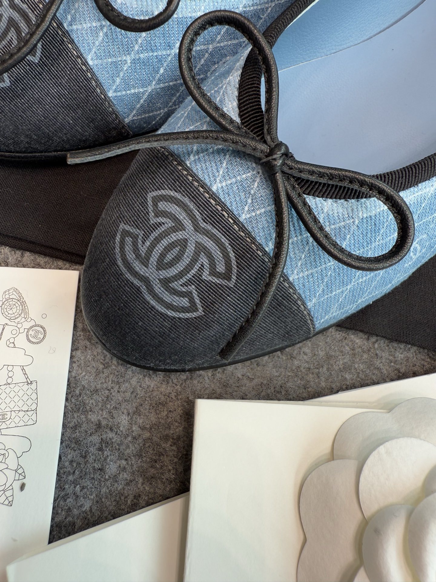 Pair of Chanel light blue quilted denim ballerina flats with black toe caps and bows inside a white luxury box. - Hình 6