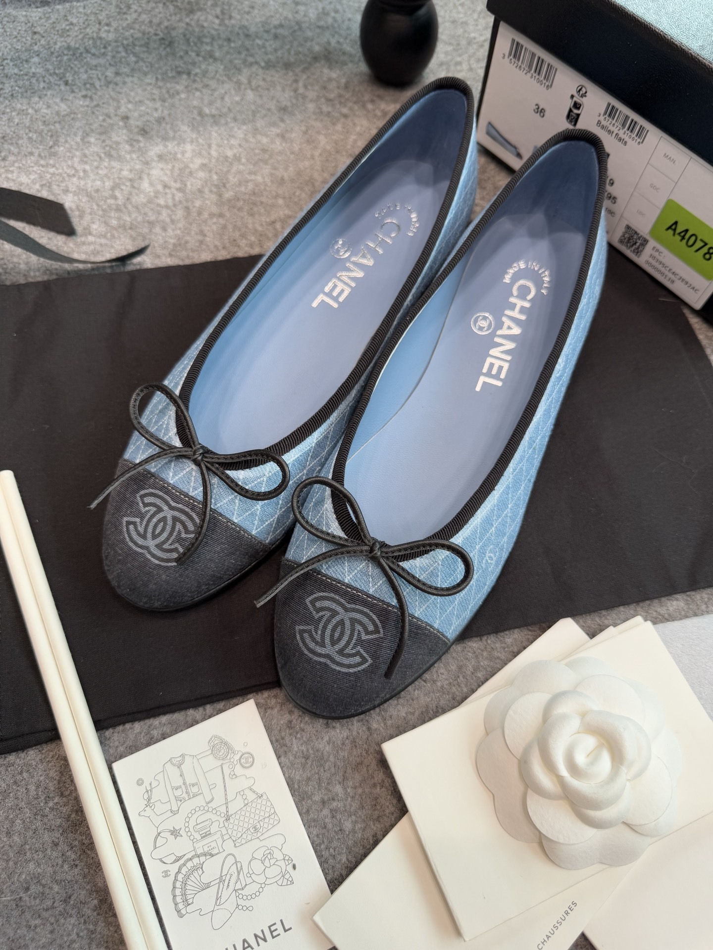 Pair of Chanel light blue quilted denim ballerina flats with black toe caps and bows inside a white luxury box. - Hình 5
