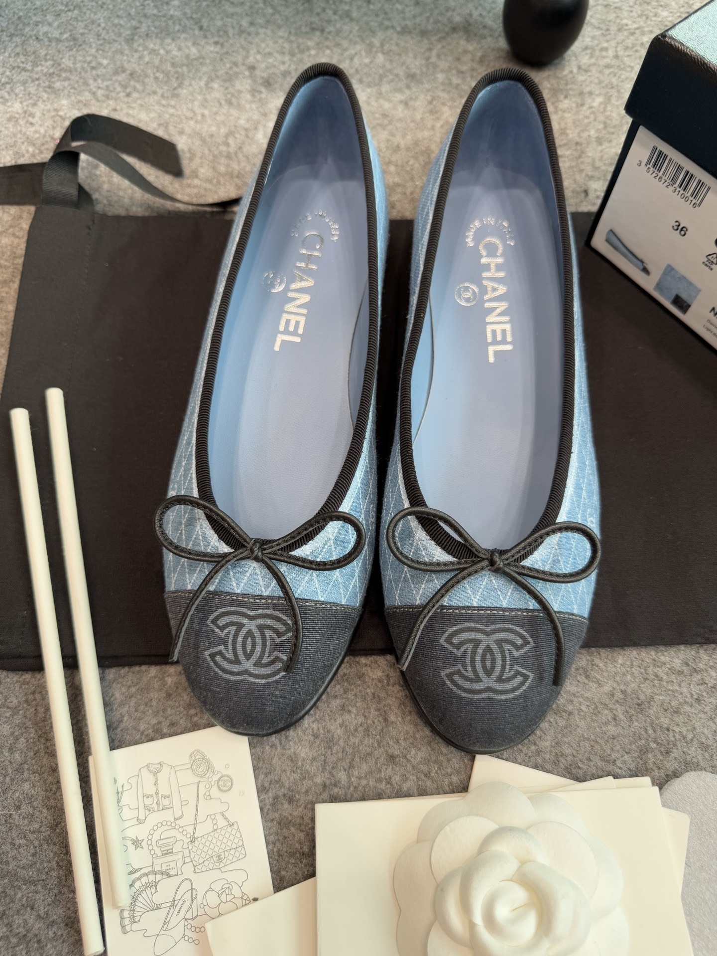 Pair of Chanel light blue quilted denim ballerina flats with black toe caps and bows inside a white luxury box. - Hình 4
