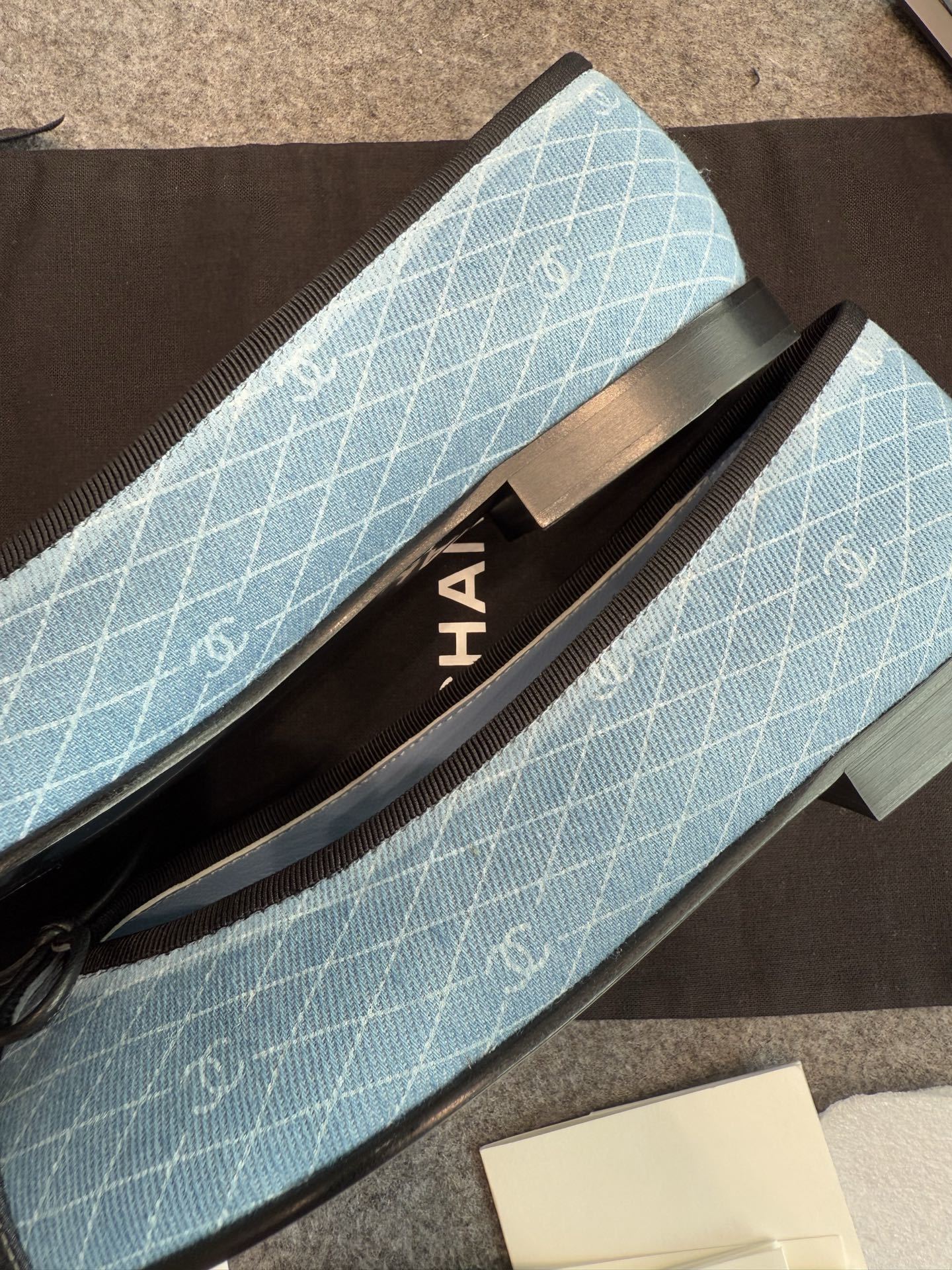 Pair of Chanel light blue quilted denim ballerina flats with black toe caps and bows inside a white luxury box. - Hình 3