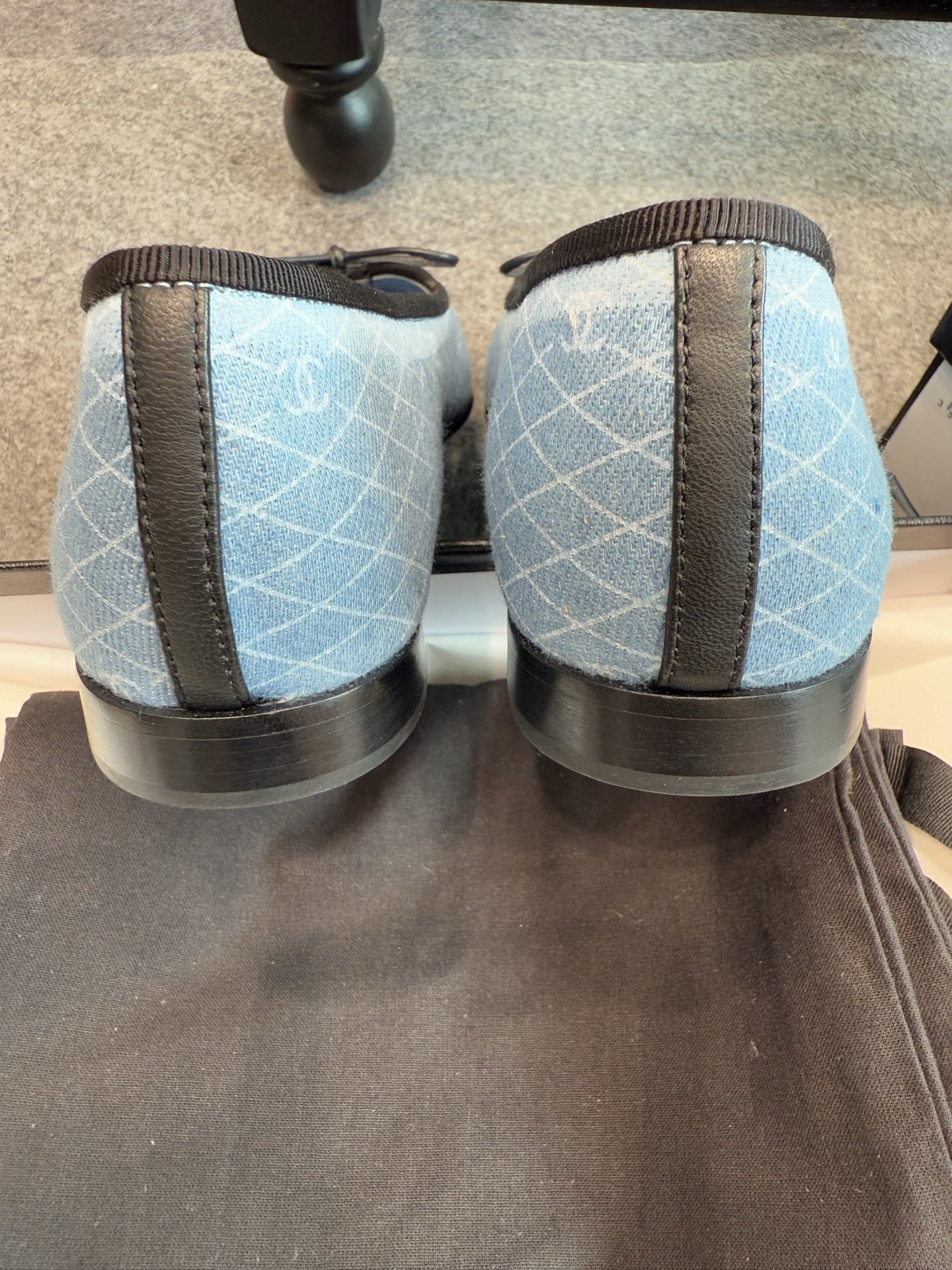 Pair of Chanel light blue quilted denim ballerina flats with black toe caps and bows inside a white luxury box. - Hình 2