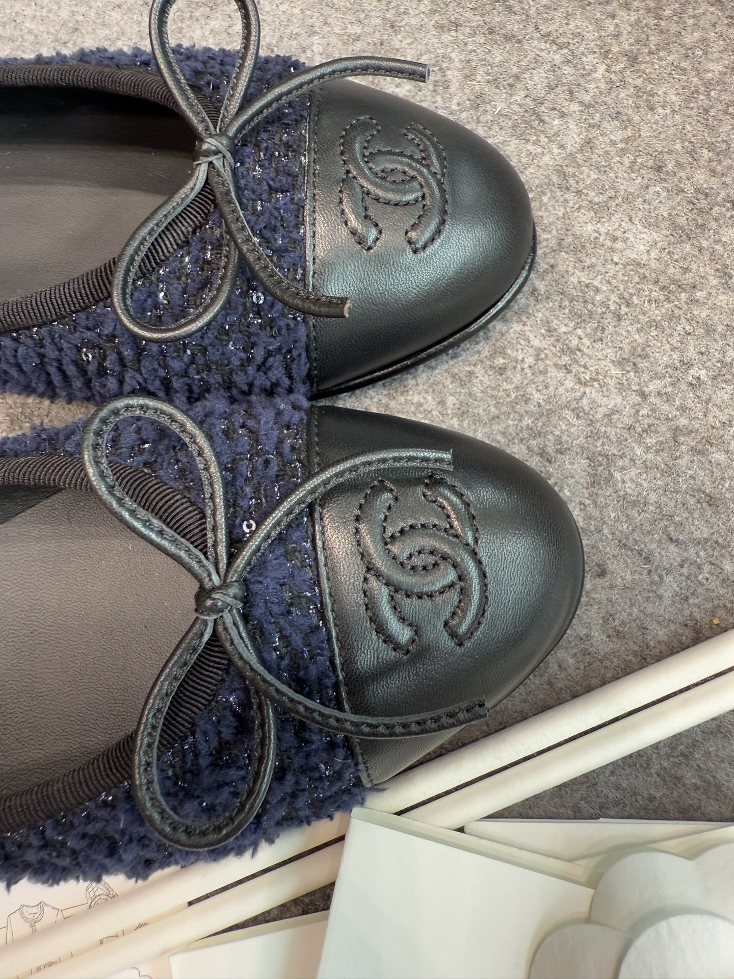 A pair of Chanel dark blue tweed ballet flats with black leather toe caps and CC logo, shown with original box and packaging. - Hình 7