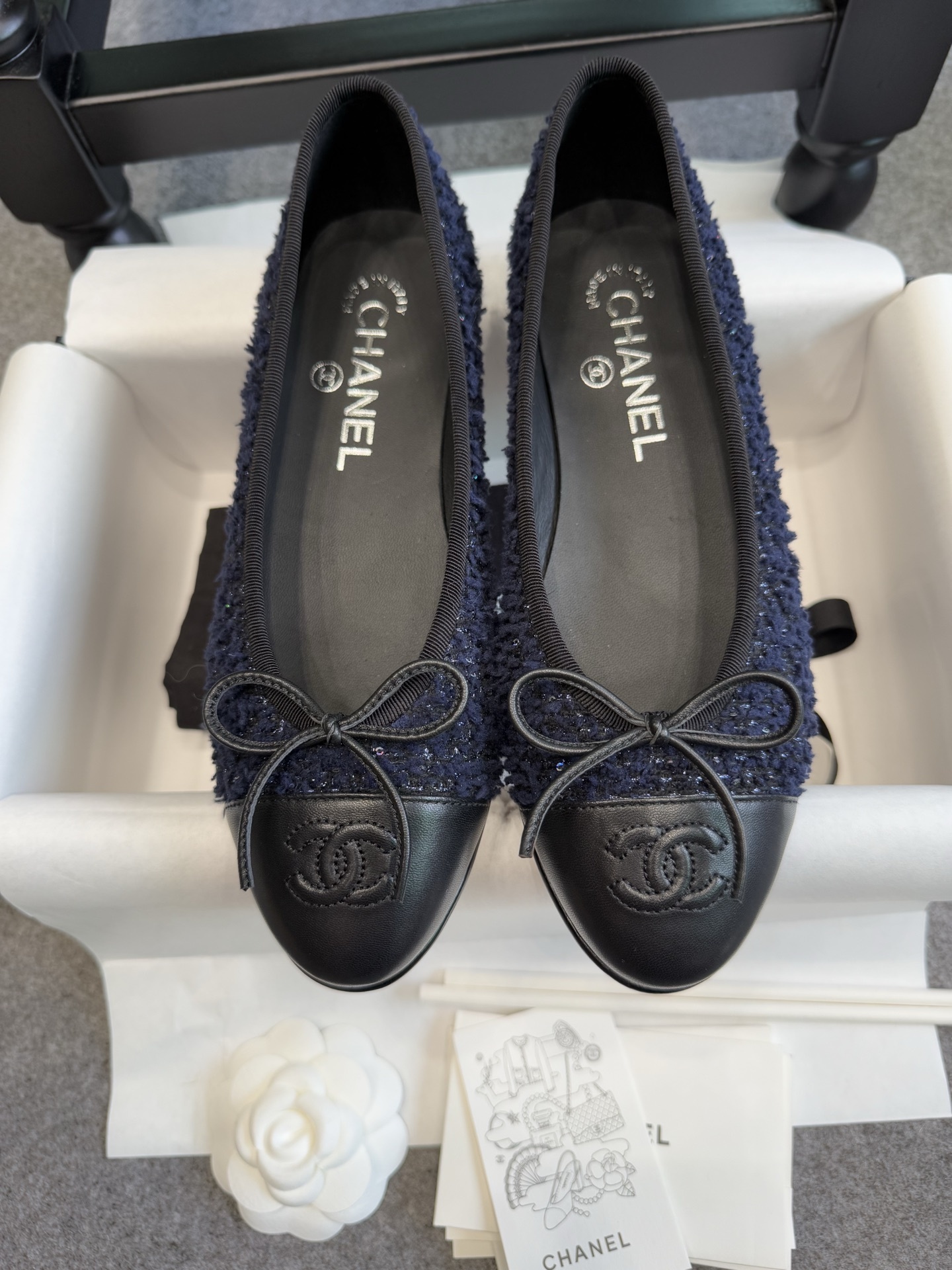 A pair of Chanel dark blue tweed ballet flats with black leather toe caps and CC logo, shown with original box and packaging. - Hình 3