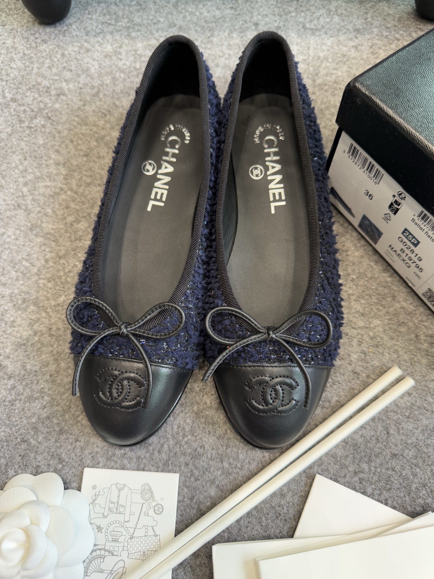 A pair of Chanel dark blue tweed ballet flats with black leather toe caps and CC logo, shown with original box and packaging. - Hình 2