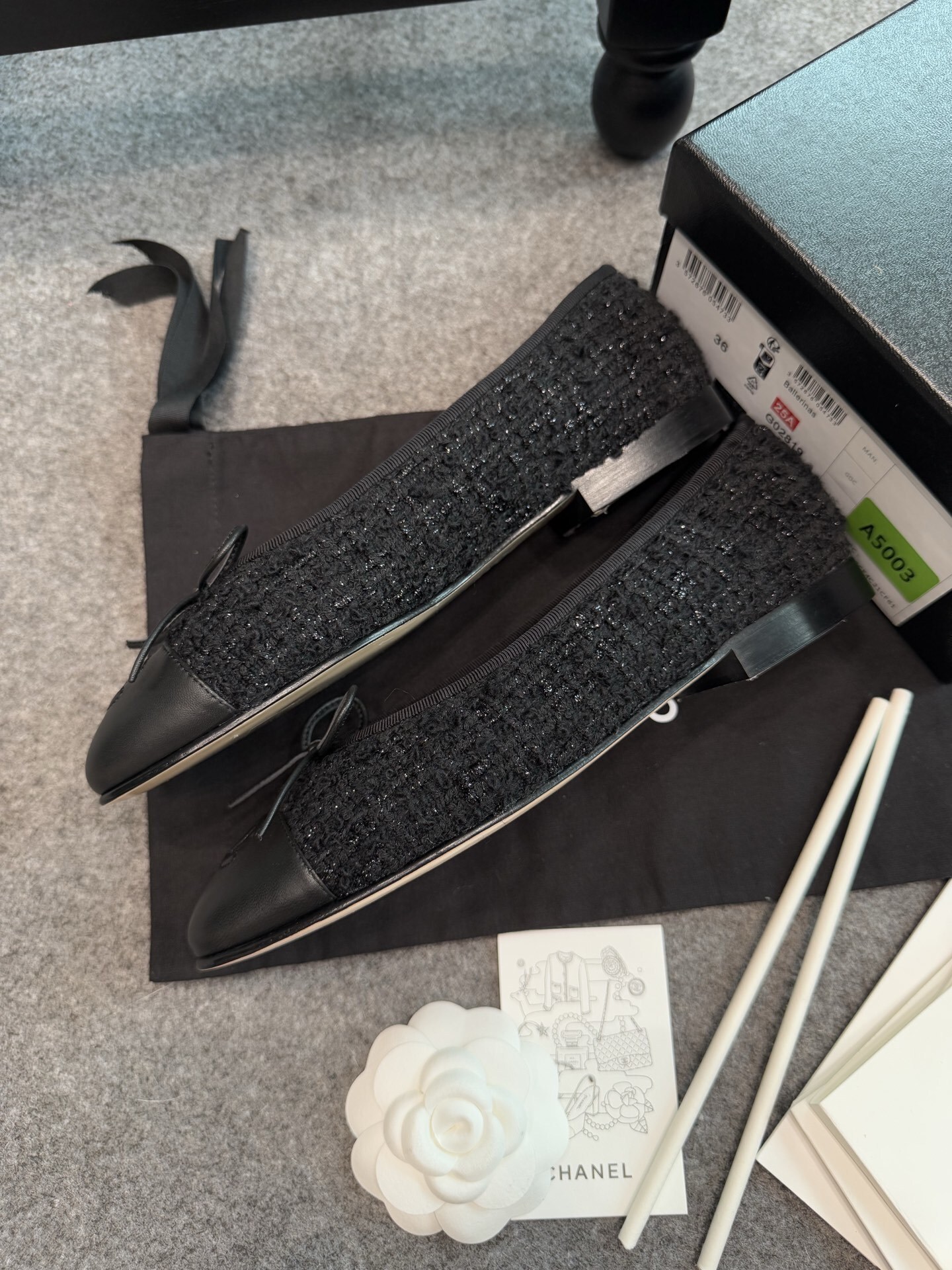 A pair of black Chanel tweed ballerina flats with leather CC logo toe caps and bow details inside a luxury box. - Hình 9