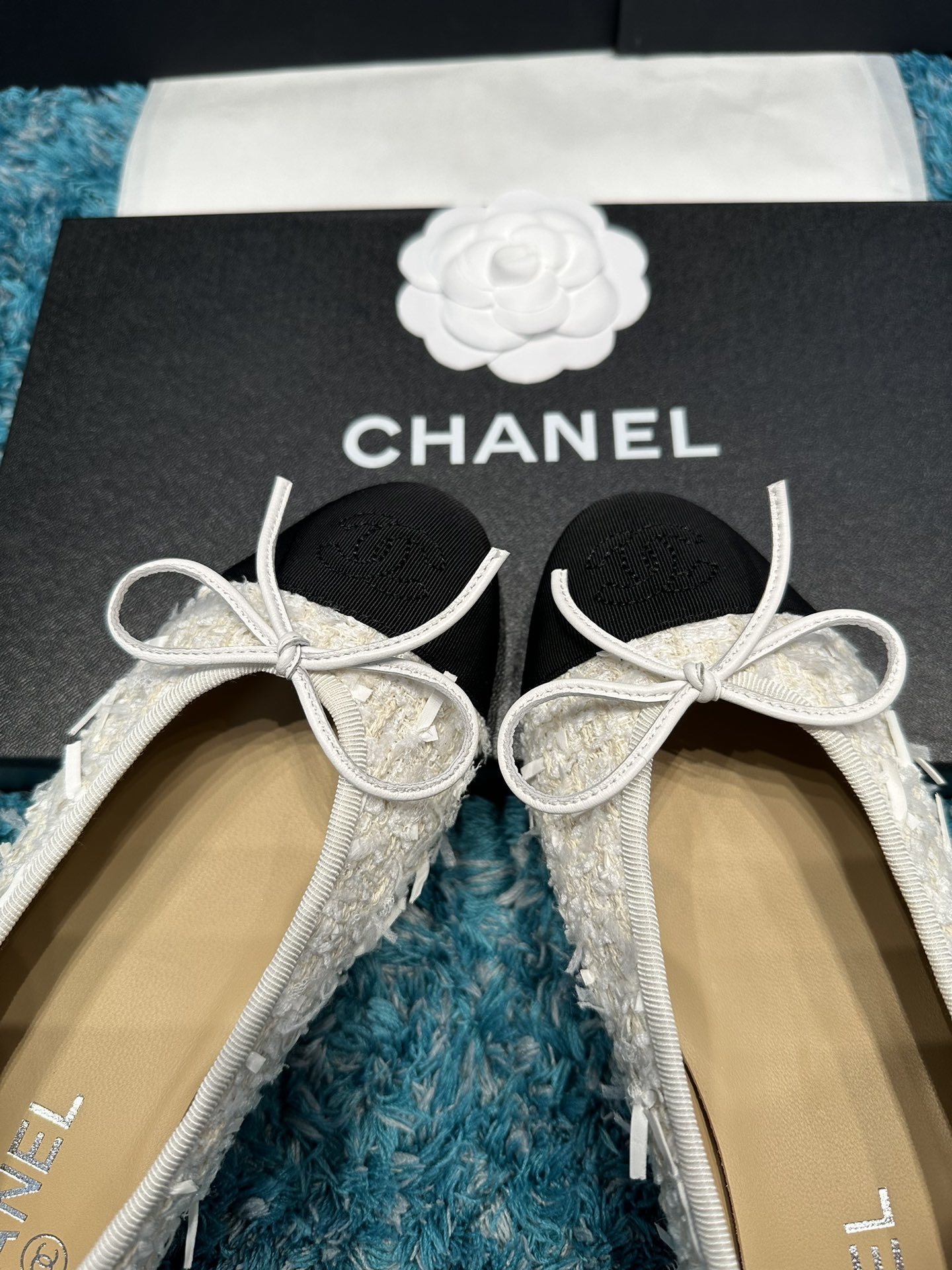 A pair of Chanel white tweed ballet flats with black toe caps and white bows, presented in a Chanel box with branded ribbons. - Hình 3