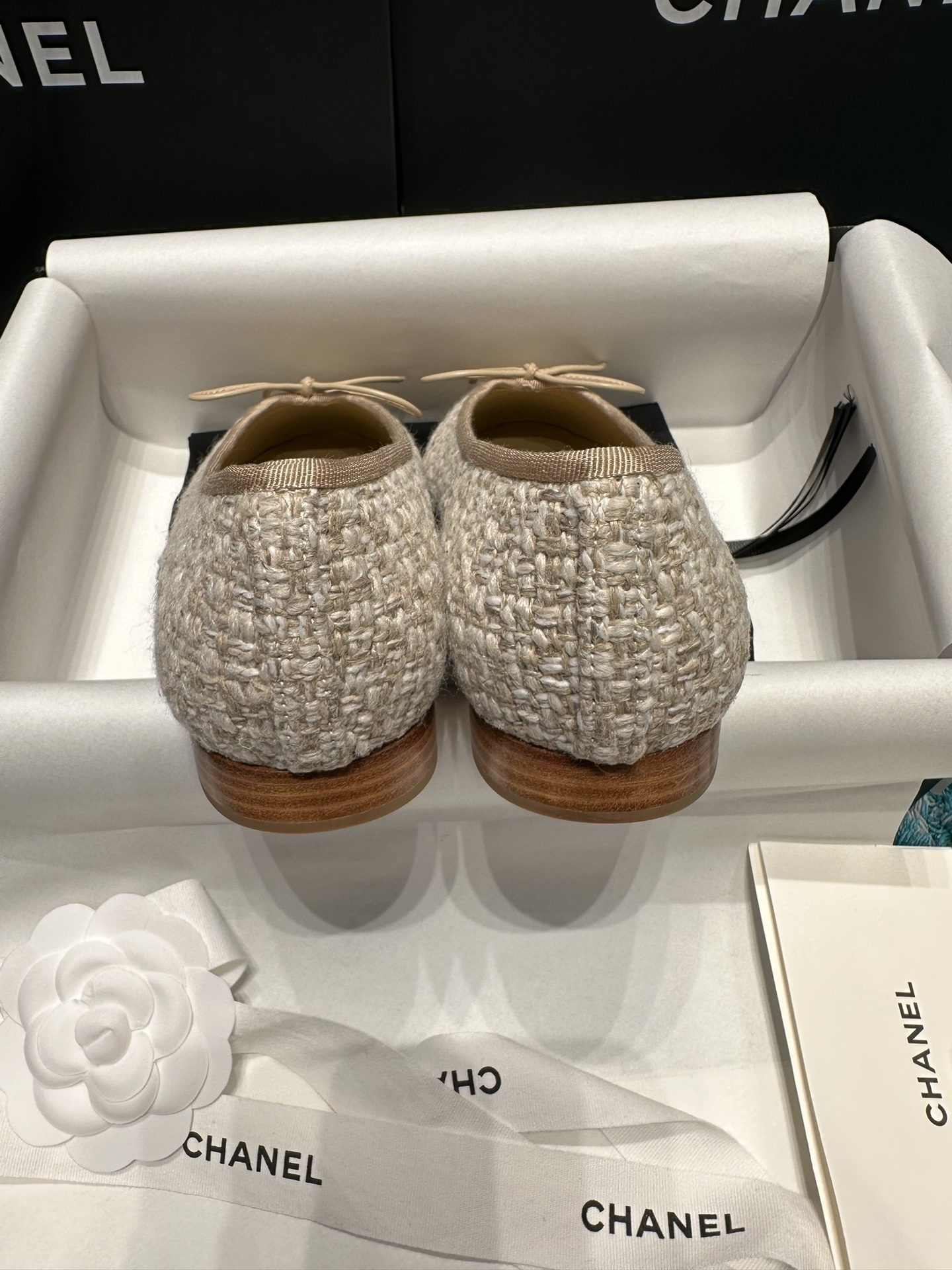 A pair of Chanel beige tweed ballet flats with a leather toe cap featuring the stitched CC logo and a small bow, presented in their original luxury packaging. - Hình 8